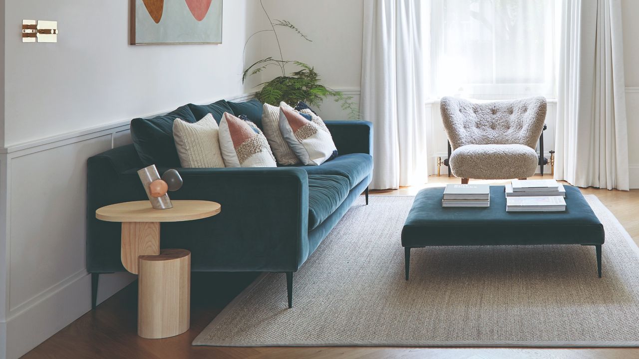 A living room with a teal velvet sofa and a matching ottoman for a coffee table and a small side table