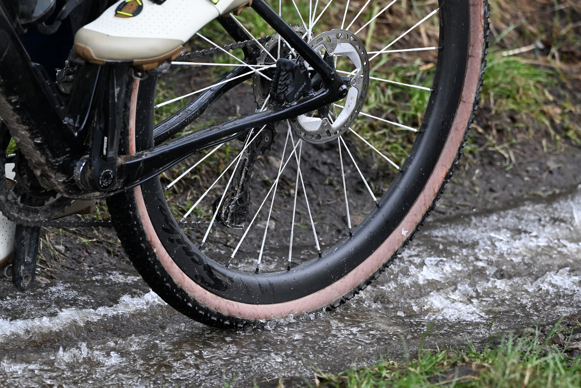 Close up of a gravel bike rear wheel being ridden through an icy puddle