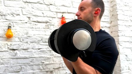 James Frew working out with adjustable dumbbells in front of a white painted wall