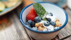 Bowl of yoghurt, fruit and granola on wooden table