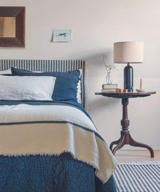Double bed with cream and blue bedding against a grey wall.