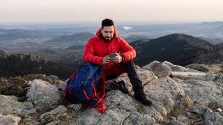 Man sitting on rocky mountain checking smartphone