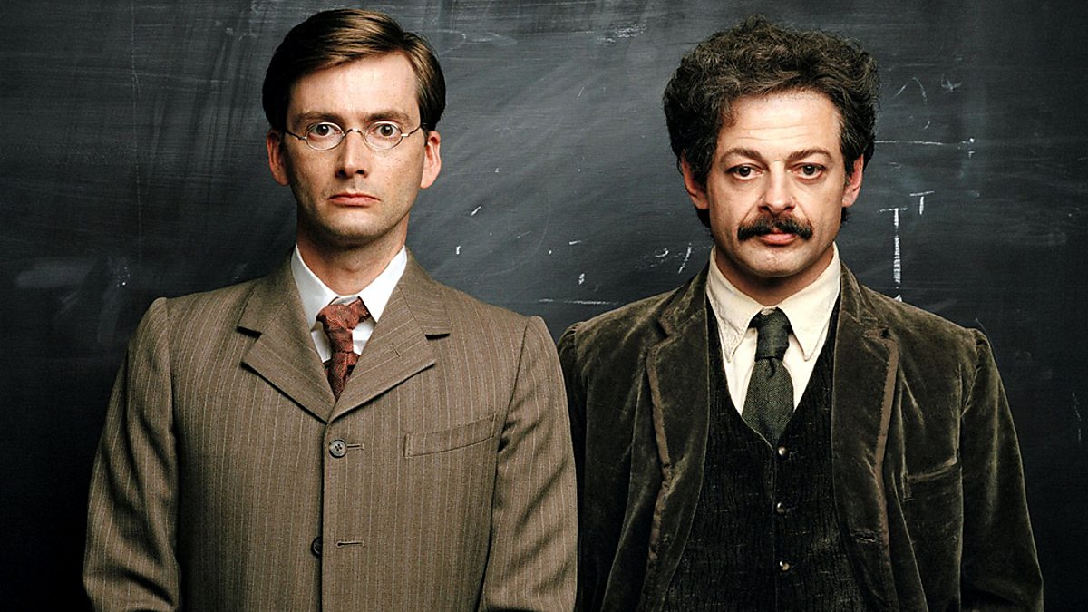 A publicity still from the BBC drama Einstein and Eddington shows David Tennant as Eddington and Andy Serkis as Einstein, standing together in period suits in front of a chalkboard.