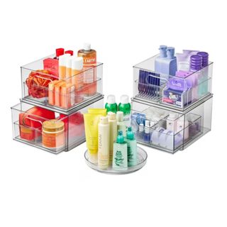 Three clear acrylic bathroom organizers filled with orange, purple, yellow and green bottles and tubs