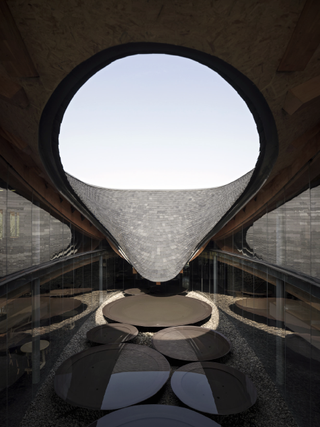 The Inkstone House is an extraordinary construction. The roof is curved and open in the center in the middle. The opening is in the shape of an upside-down raindrop that almost touches the floor, which is covered in brown circular 'stepping stones'.