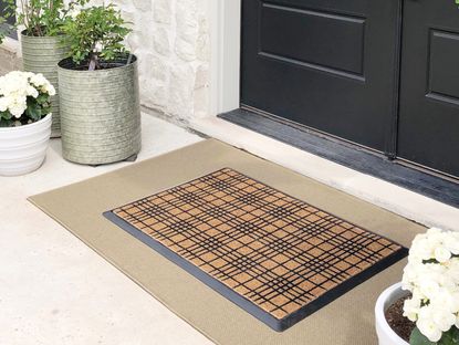 A close up of a patterned doormat in a doorway surrounded by potted plants