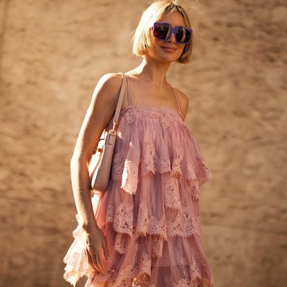 a fashion week attendee with blonde bob wears sunglasses, pink ruffled dress