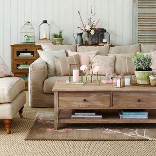A neutral living room with sofa loaded with patterned cushions and low wooden coffee table