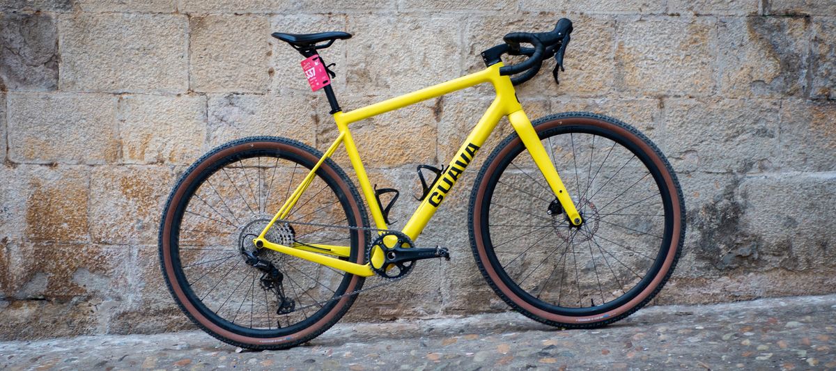 A yellow Guava Spot gravel bike leans against a wall