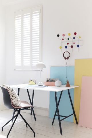 an all-white office with black metal and white desk and chair, and pops of color in the form of color pieces of cardboard, and lots of colored hooks