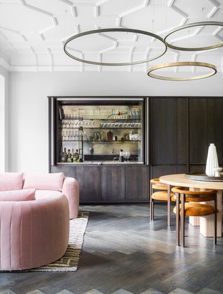 open plan living room with pink sofa, dining table and home bar