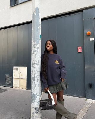 French woman wearing miniskirt, tall boots, and oversize crewneck