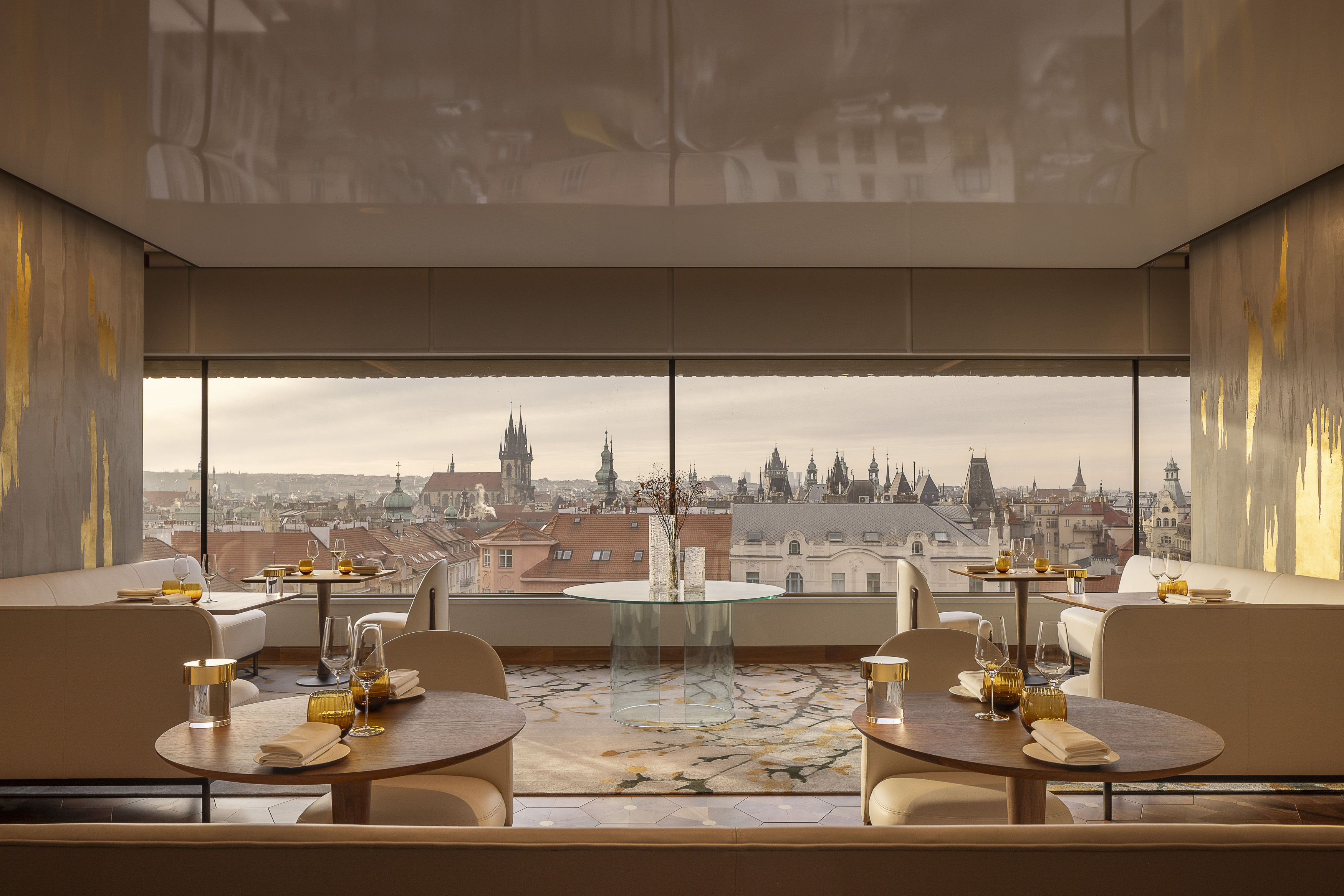 A hotel lounge dressed in luxurious furnishings overlooks a historical city at sunset.