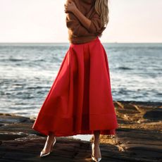 A woman in a red skirt and brown top next to the ocean.