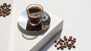 An espresso on a white countertop in a small glass mug with coffee beans around it