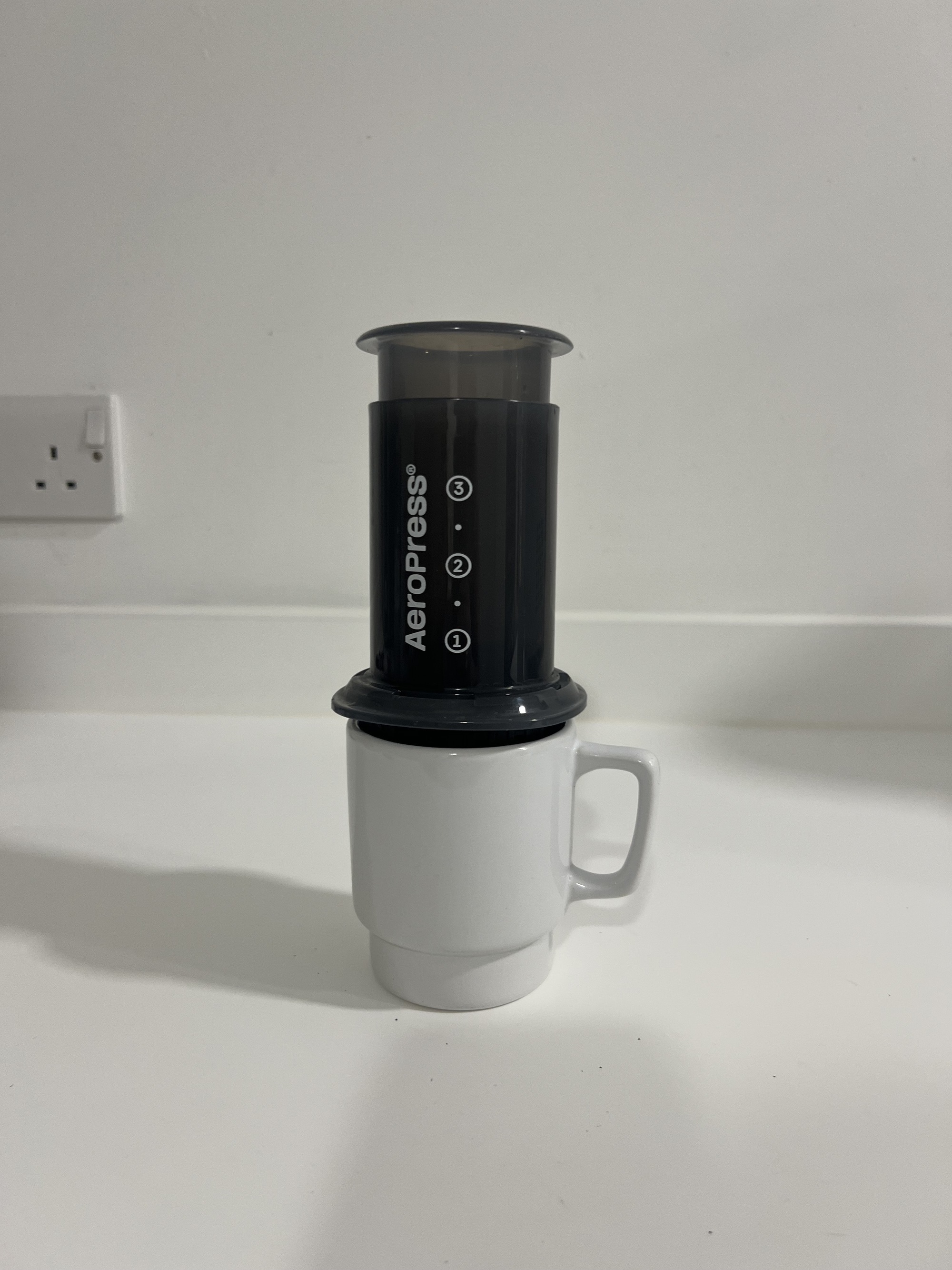 Image of a black AeroPress machine on top of a white coffee mug on a white kitchen countertop.