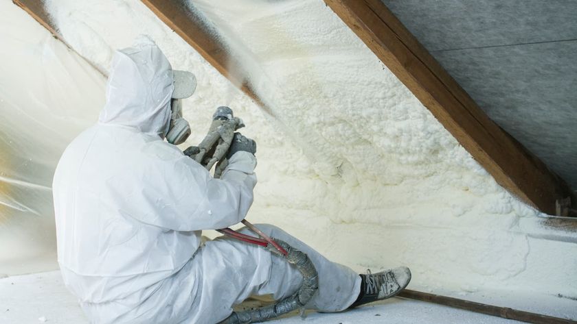 technician spraying foam insulation using plural component gun for polyurethane foam, inside