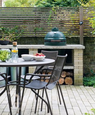 A brick-built outdoor kitchen with round black metal table and chairs.