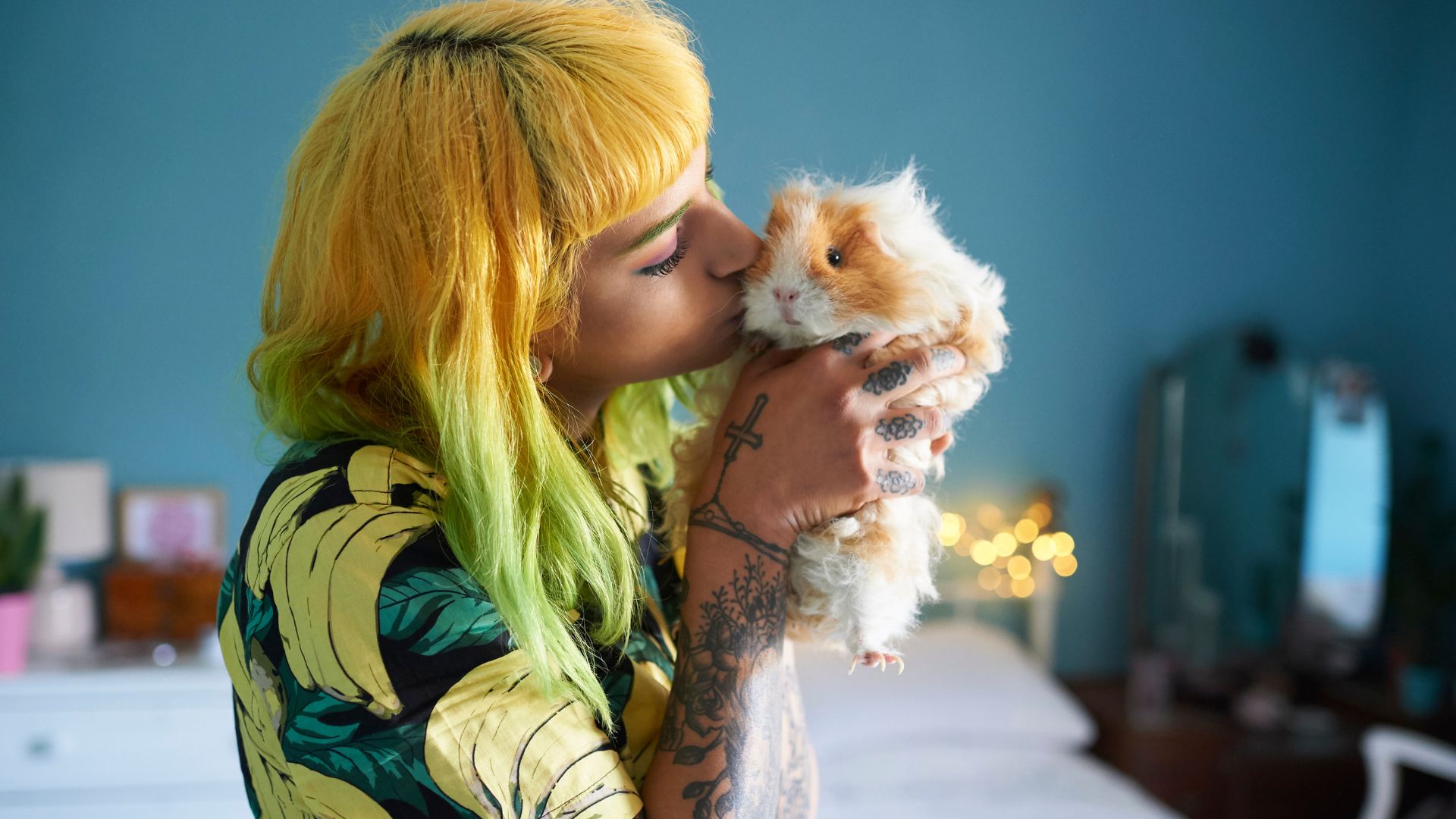 A guinea pig being kissed by a woman with orange and green hair