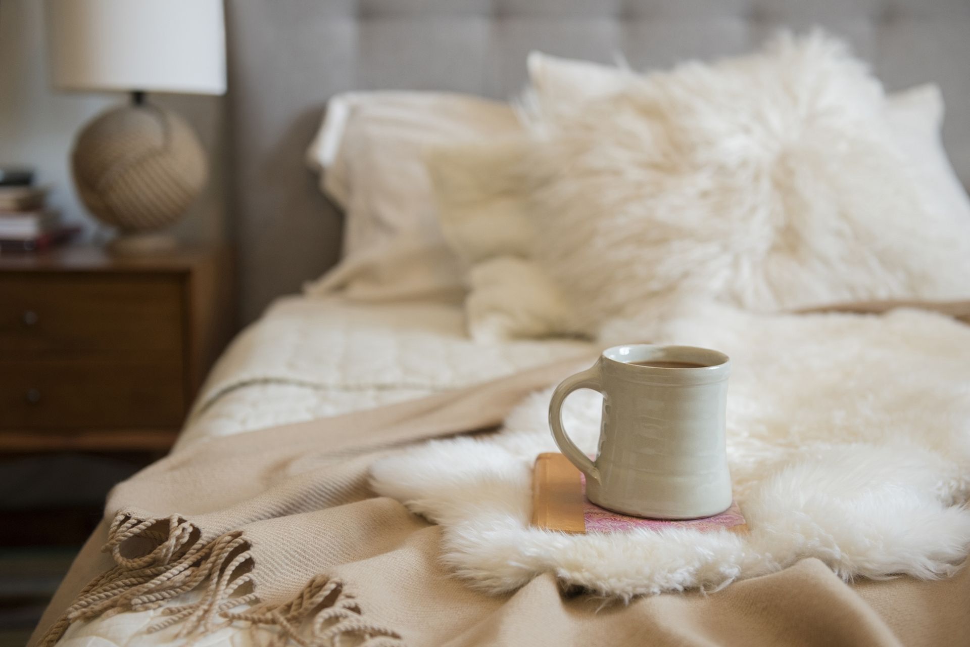 Coffee cup and book on fur on bed
