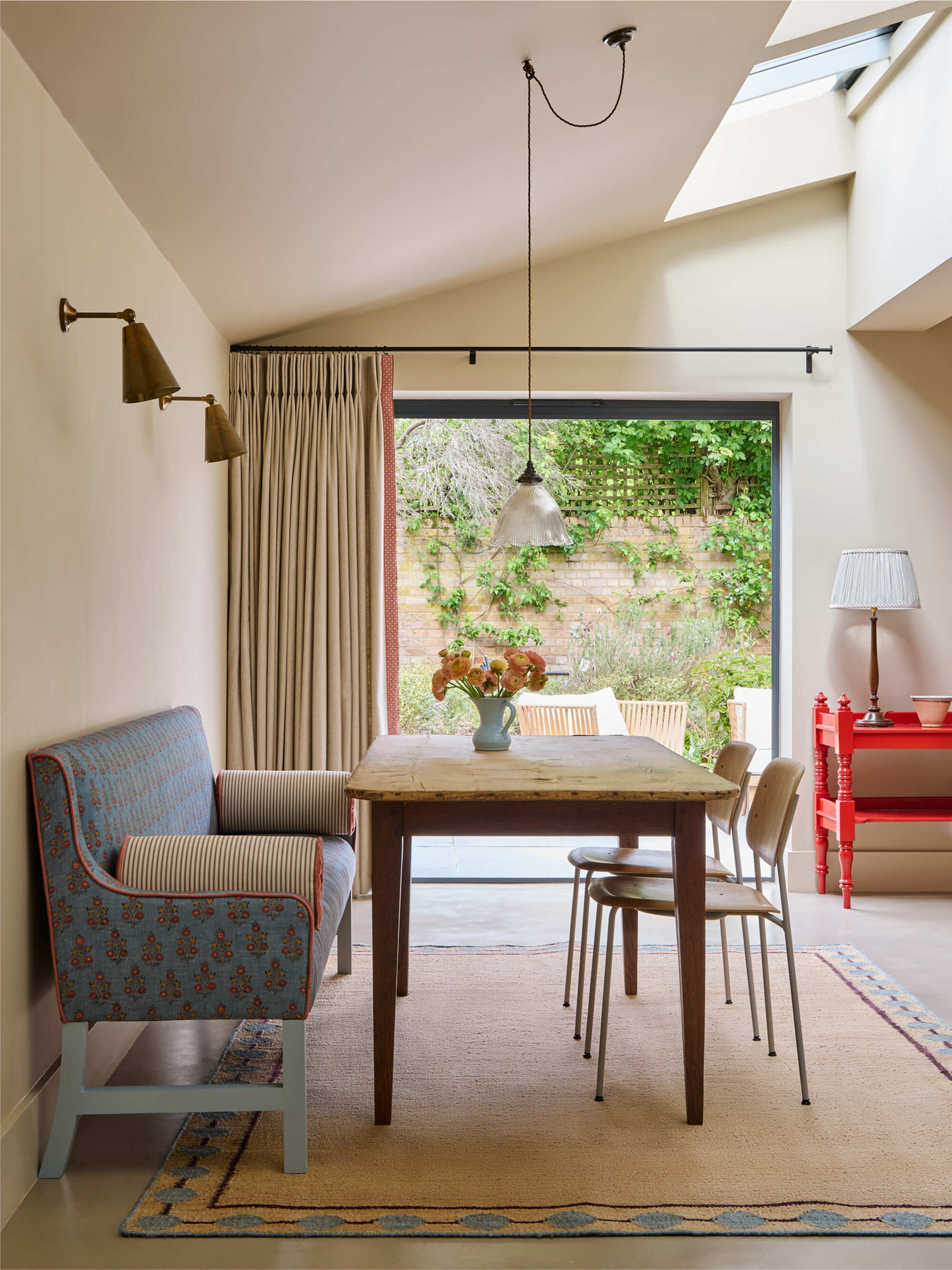modern dining area with sloped ceiling, door to outside, jute rug with patterned border, timber table, two timber dining chairs, and then fabric upholstered dining bench seat
