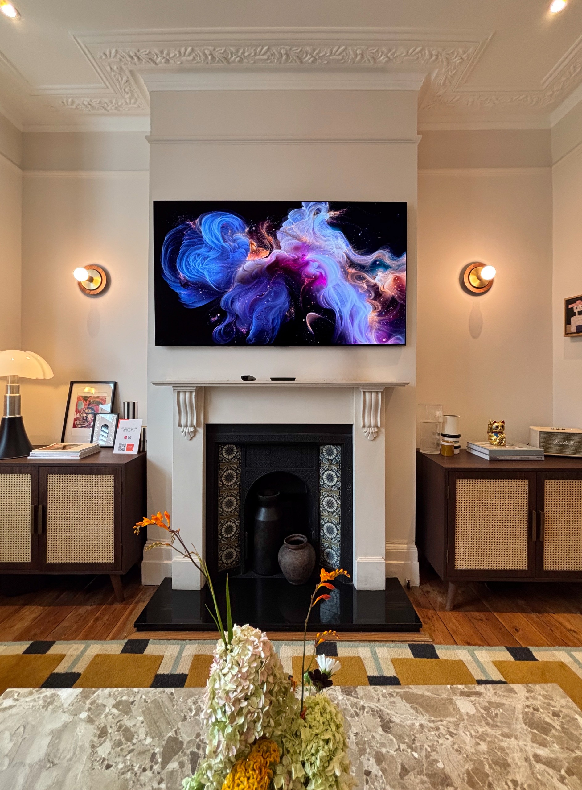 a living room in a victorian home with a fireplace, tv on the wall, and decorative moulding 