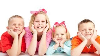 Four boys and girls lie on floor smiling broadly into camera.