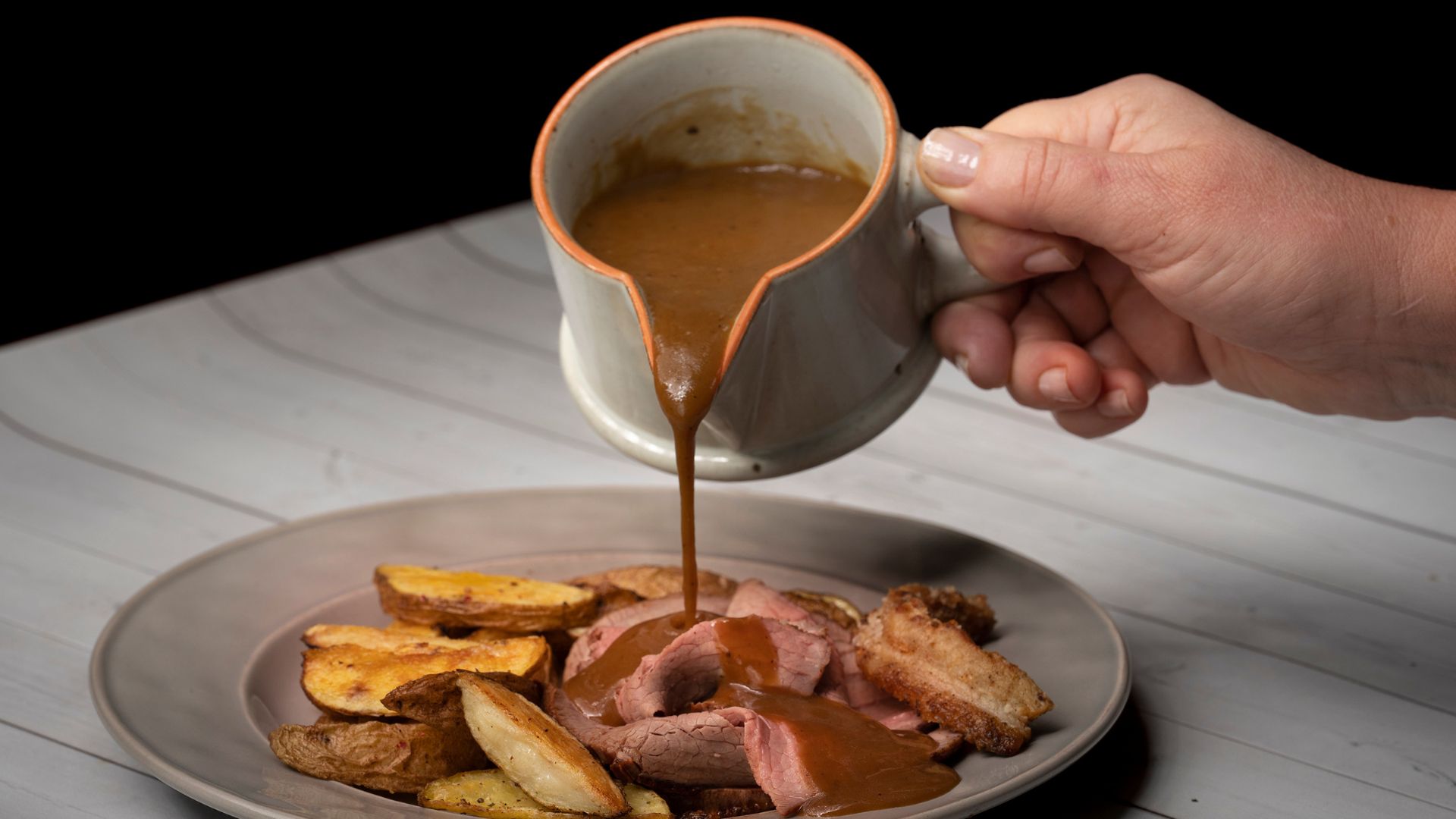 Gravy being poured from a pot onto beef and chicken