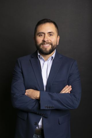 Smiling headshot of David Serpa with his arms folded in a navy suit.