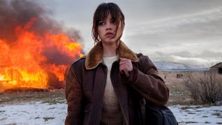 Jenna Ortega in Hurry Up Tomorrow walking away from a fire with a backpack slung over her right shoulder.