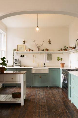 A country style kitchen with green cabinets, wooden floorboards and open shelving