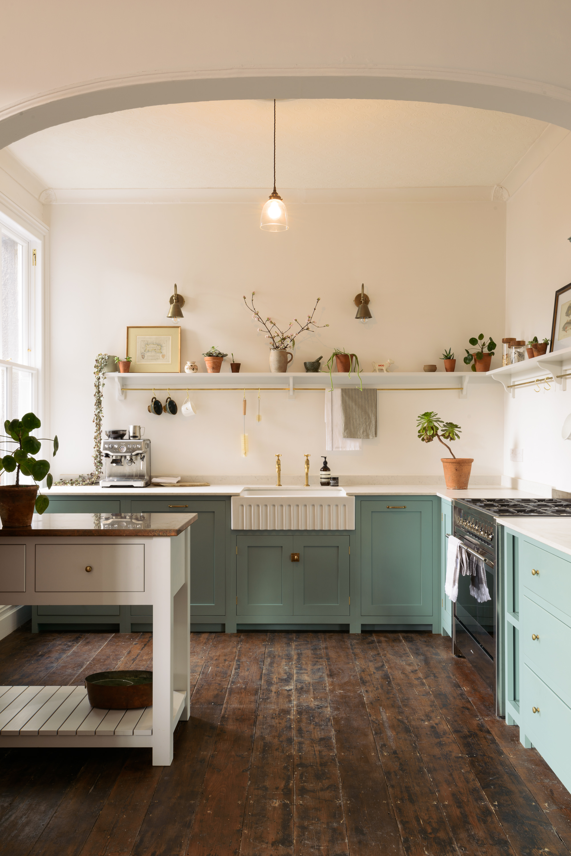 A country style kitchen with green cabinets, wooden floorboards and open shelving