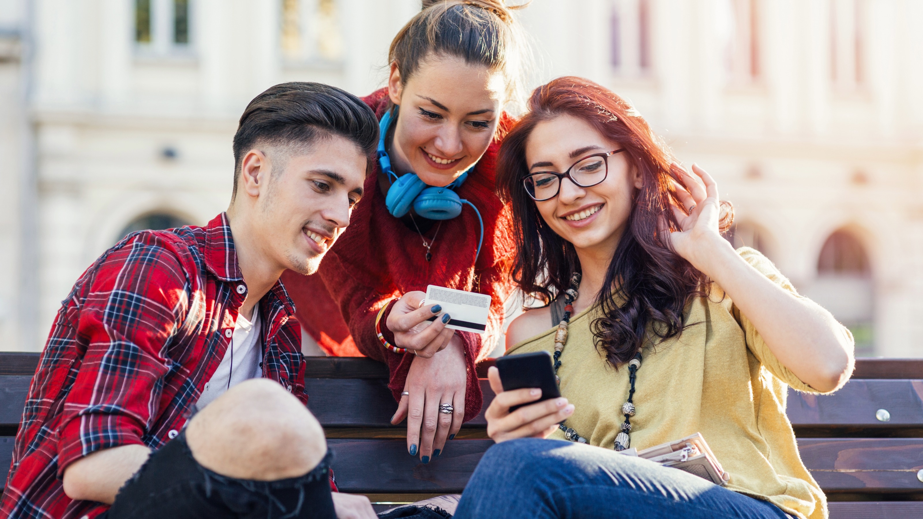 Three friends on the street bench using bank card online