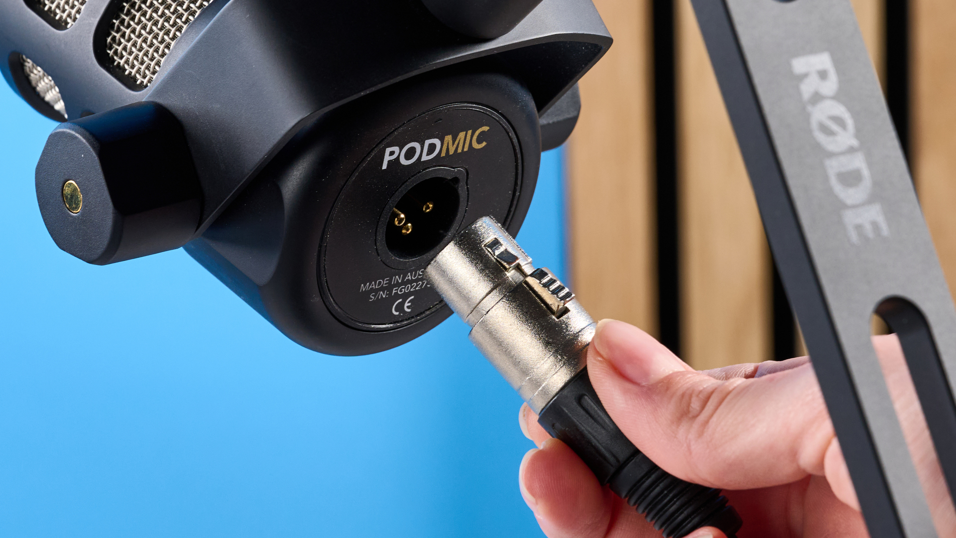 the rode podmic podcast and broadcast microphone photographed with a blue background, shown with the rode ds2 desk stand