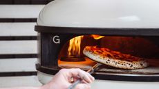 putting a pizza into a lit outdoor pizza oven 