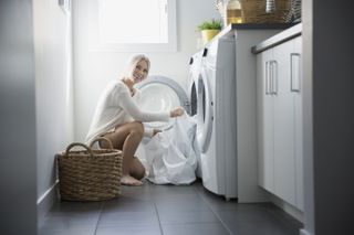 woman putting white sheets into washing machine