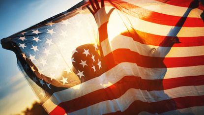 Rear view of a couple holding American flag against sunset