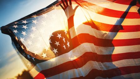 Rear view of a couple holding American flag against sunset