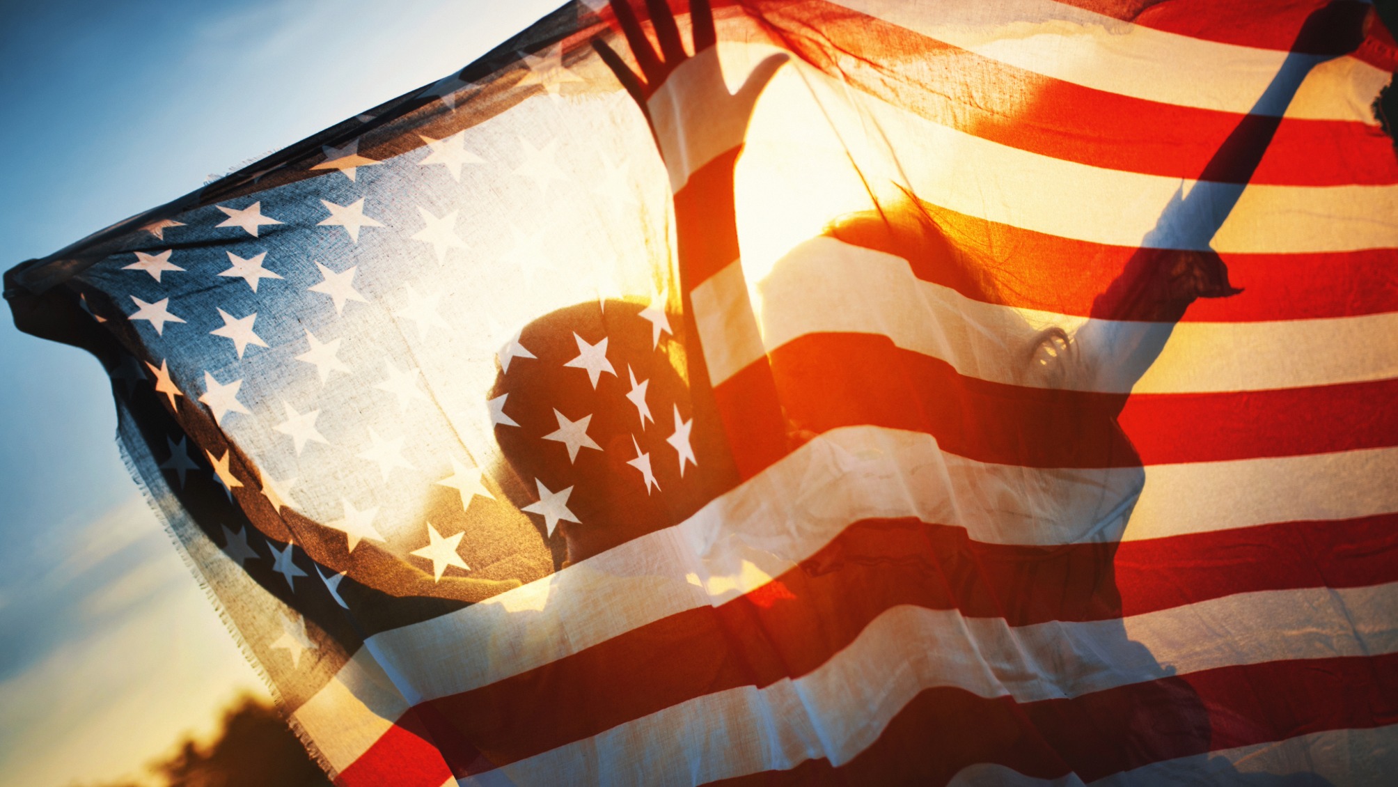 Rear view of a couple holding American flag against sunset