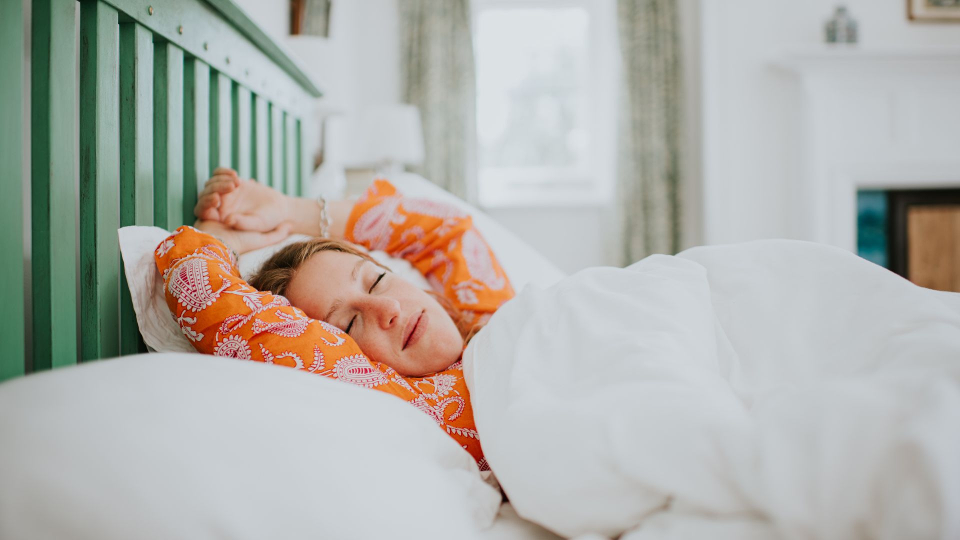 A woman lies happily asleep in bed with her arms above her head.