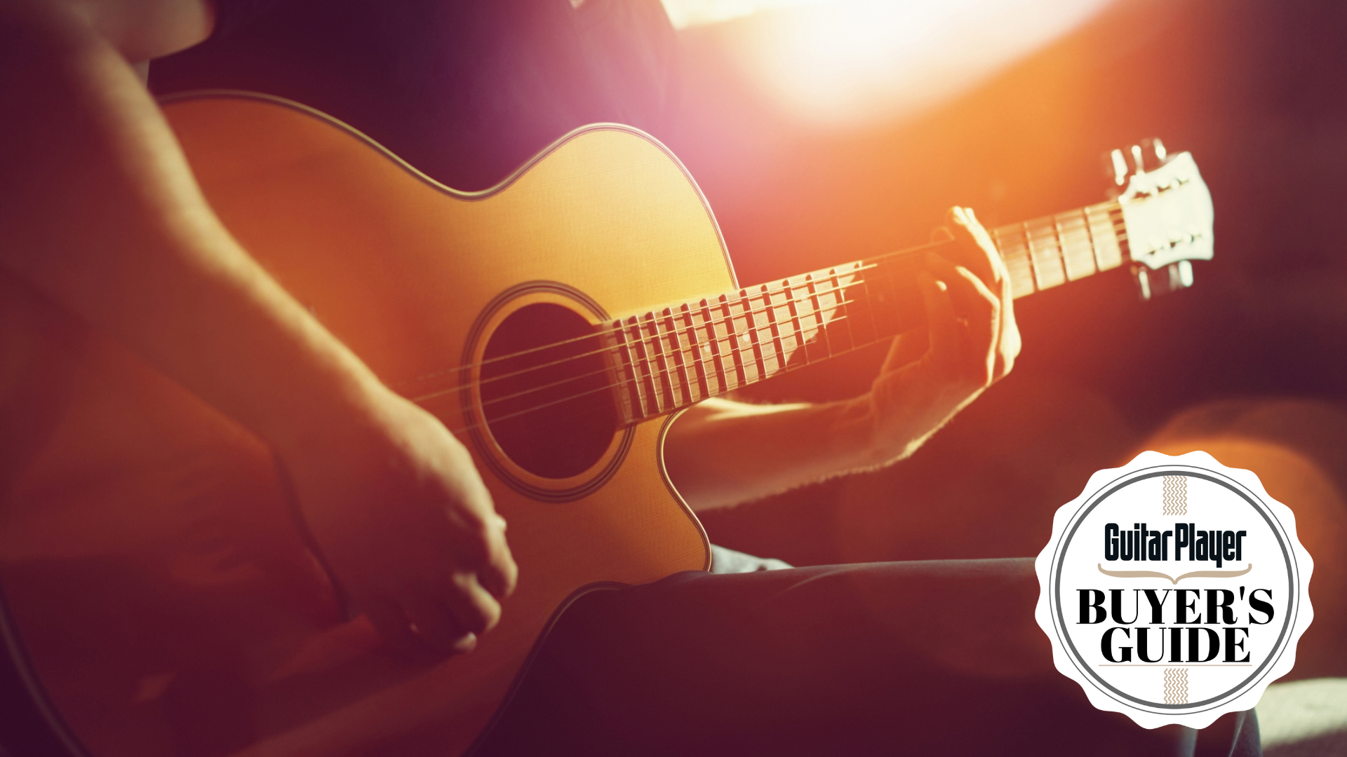 Young guitarist in a black t-shirt bathed in orange light and holding an acoustic guitar