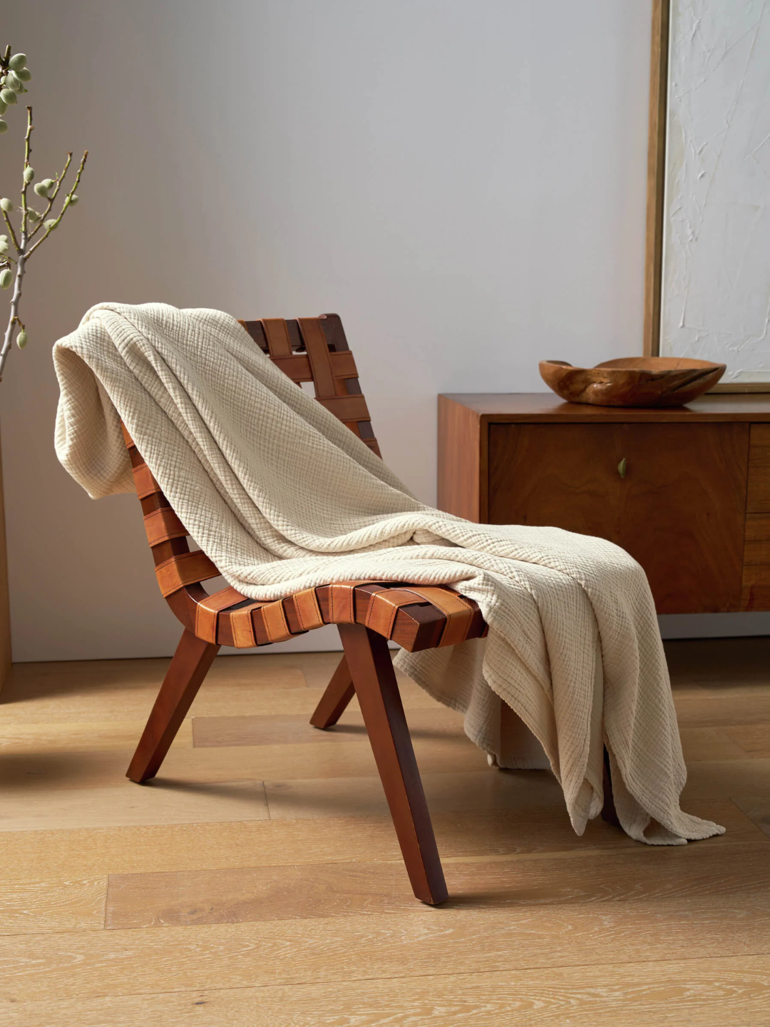 A coconut colored cottan gauze blanket from Cozy Earth draped on a curved wood chair