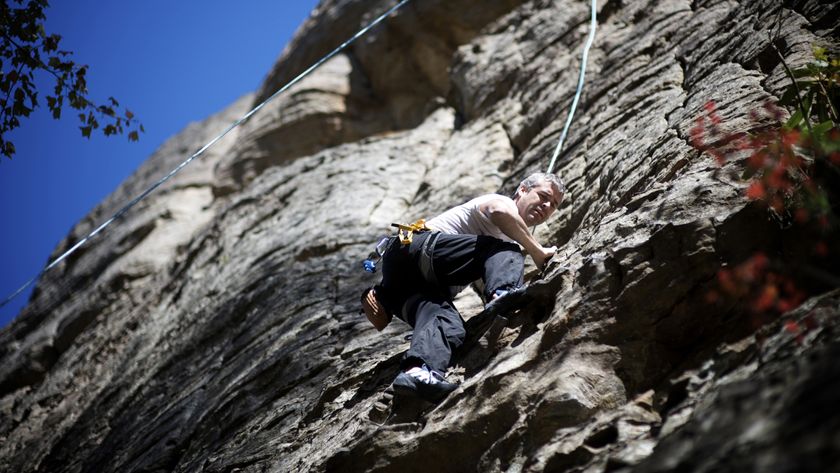 A male rock climber climbs a limestone rock face in the Red River Gorge, KY on a warm Fall day