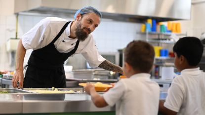 A school chef serves cooked hot dinner to students on their lunch break 