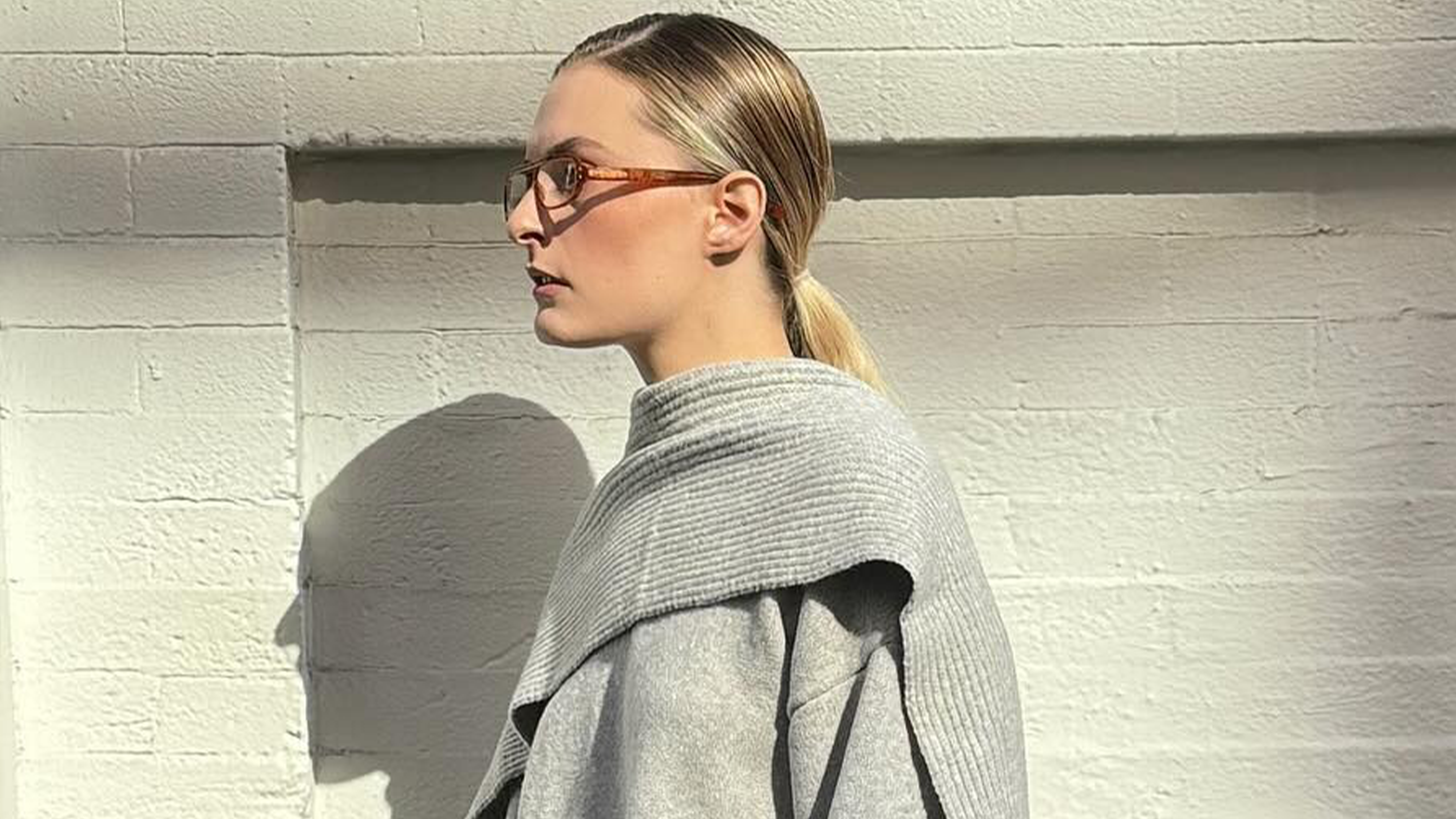 Influencer wearing gray cozy winter sweater, standing against wall.
