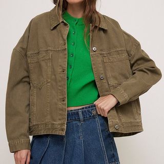 A model wears a khaki utility jacket over a green cardigan and denim skirt