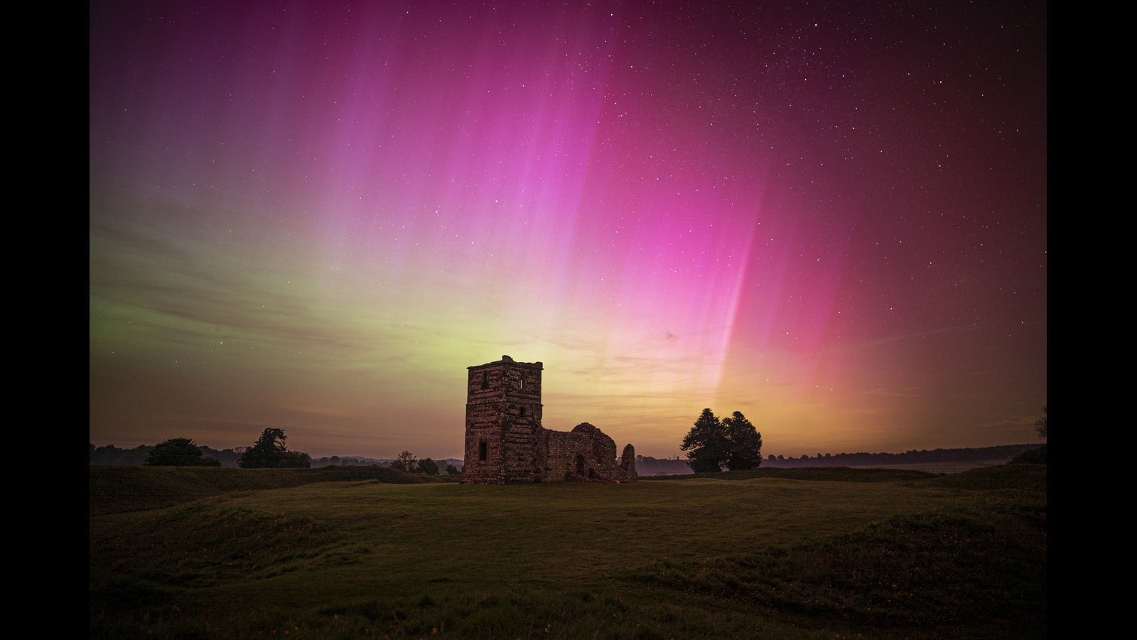 Vivid pink and purple aurora can be seen dancing in a starry night sky above an old church.