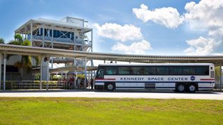 a white bus with the words "kennedy space center" on its side sites in front of a small building