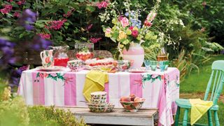 country cottage garden with table covered in pink and white stripe tablecloth with floral china and vases filled with flowers