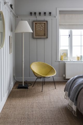 Sisal flooring in a white bedroom by Alternative Flooring, yellow chair, shiplap walls, artwork on the walls, pops of yellow, stripe blanket on bed, white and metal floor lamp